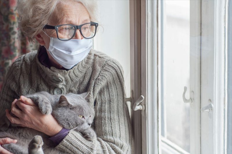 Elderly,Woman,In,Protective,Mask,Holding,A,Cat,Looks,Out